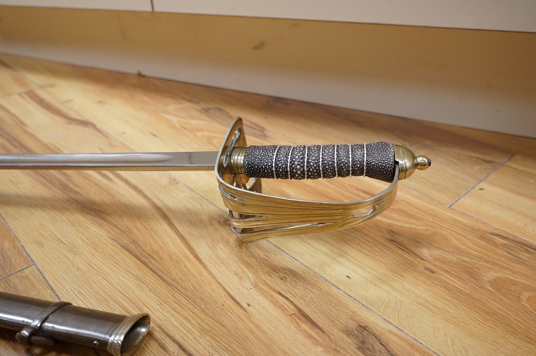 A post 1902, 1827 pattern Rifle Brigade officer’s dress sword, with regulation blade with traces of edge decoration, regulation nickel guard with crown strung bugle and wire bound fish skin covered grip, in its steel sca